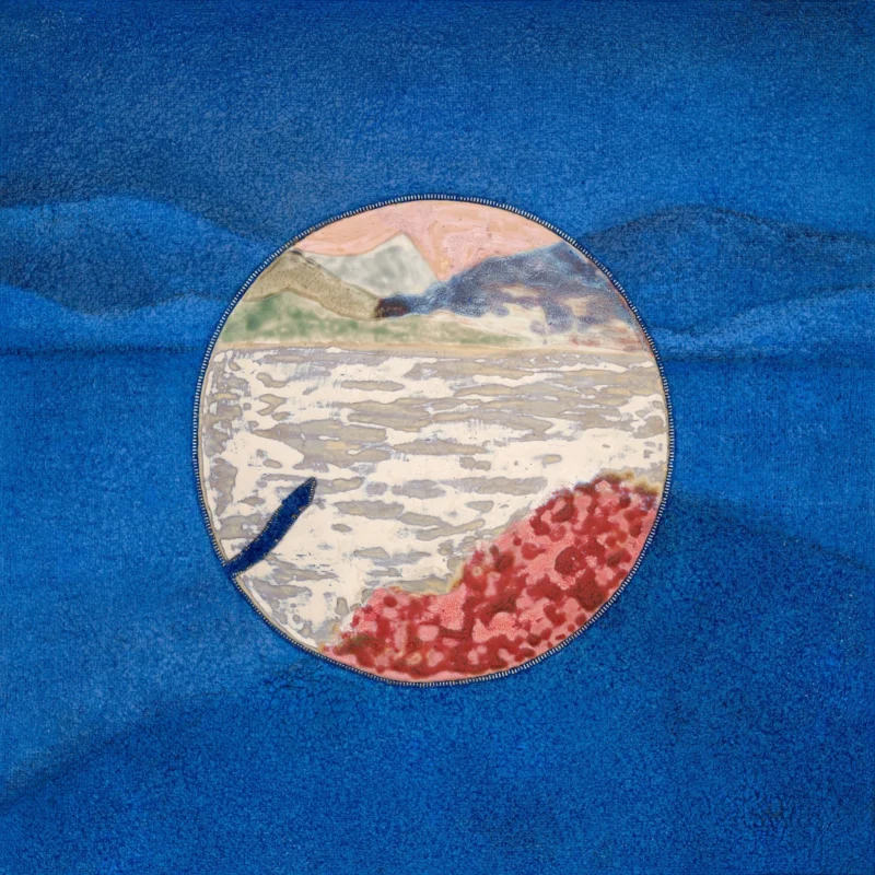 circular ceramic element embedded in deep blue textile surface, strong contrast, abstract landscape motif 円形の陶片を青い布地に埋め込んだ作品、強いコントラスト、抽象風景