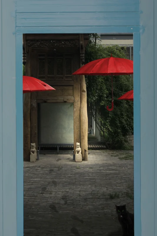 Two red umbrellas framed by architectural openings in a quiet courtyard.