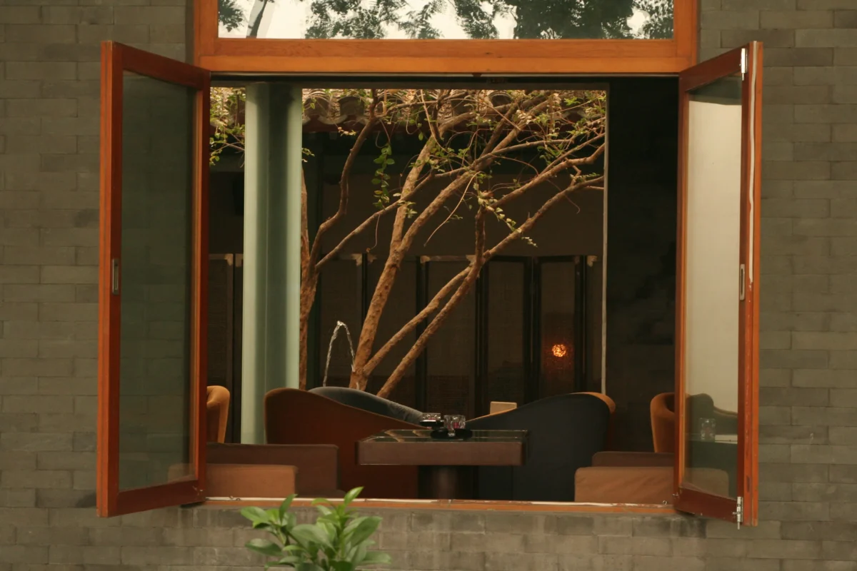 An open wooden window framing an interior space and a distant garden view.