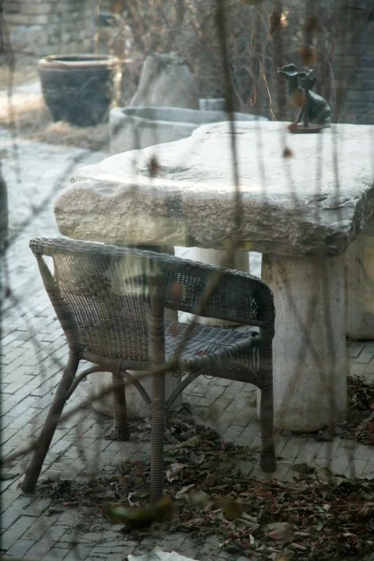 A weathered chair beside a window overlooking a quiet winter garden.