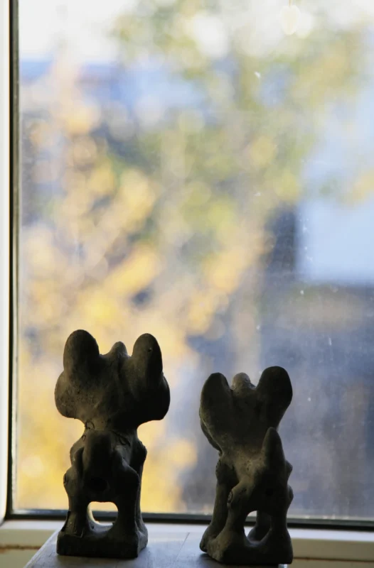 Two small figurines silhouetted against a softly blurred landscape beyond a window.