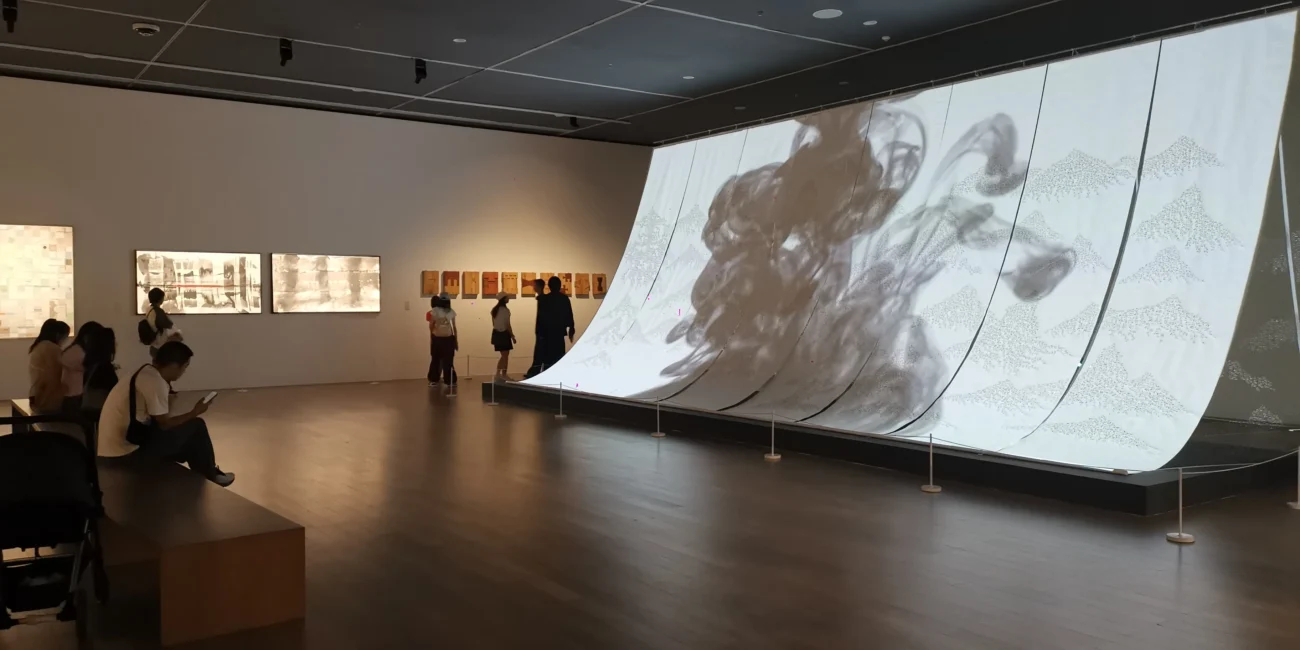 Large suspended Xuan-paper installation covered with incense-trace characters, animated ink imagery projected across its surface to create an immersive spatial landscape.