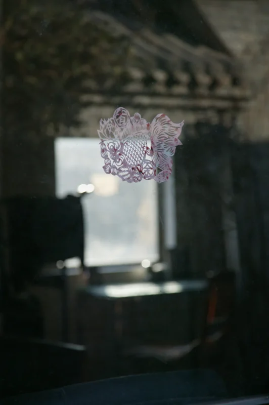 A paper-cut fish motif adhered to a glass window appears suspended before a softly blurred interior space.