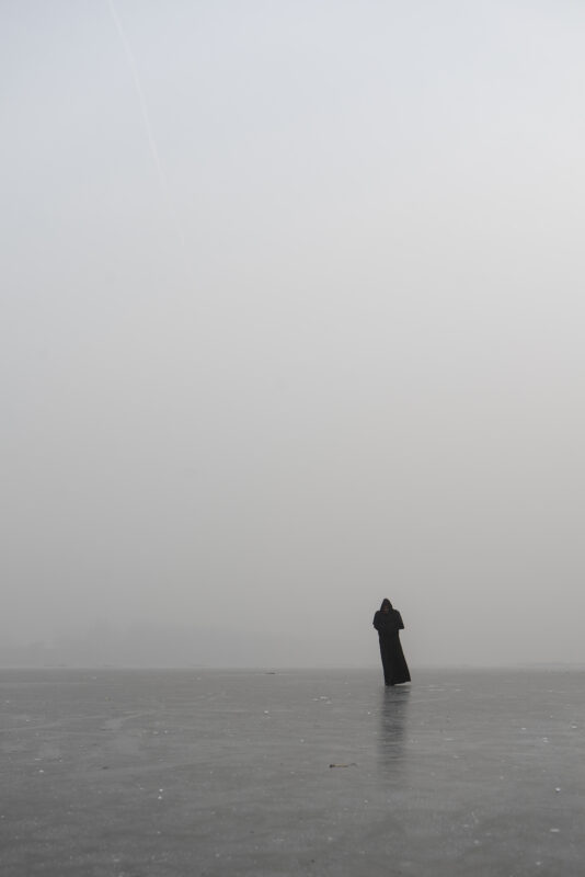 A lone figure standing in mist beside calm water in Wang Wulong’s Receding Landscape series.