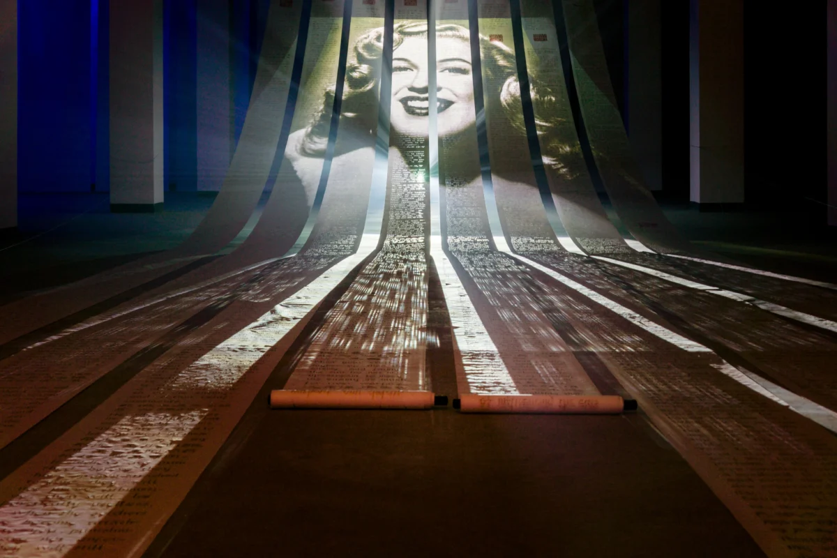 Eight suspended scrolls extending onto the floor, overlaid with a projected female portrait and incense-trace text.