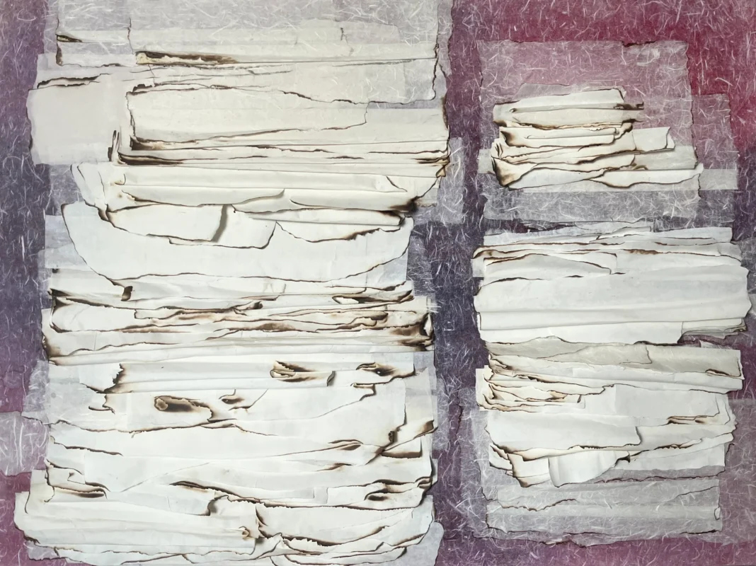 Layered handmade paper fragments arranged in stacked formations on a textured mixed-media surface.